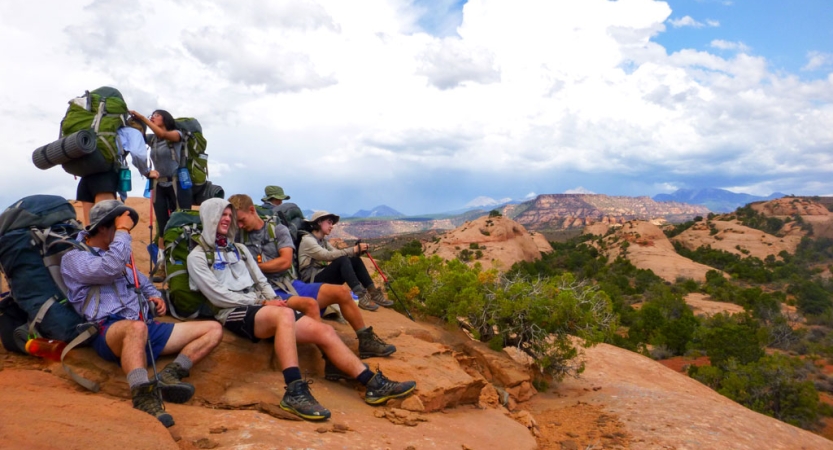 A group of outward bound gap year students wearing backpacks pose for a photo in a desert landscape